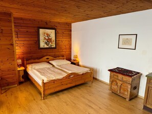 A wooden-paneled room with a bed, a nightstand, a dresser, and two framed pictures on the wall.