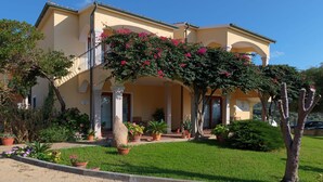 A two-story building with a balcony, potted plants, and a well-maintained lawn. - Apartment in Badus With Communal Pool (Badesi)
