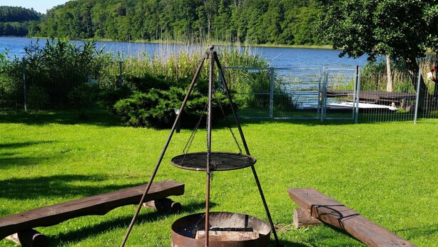 En grill av metall med ett upphängt grillgaller, två träbänkar och en eldstad med ved.