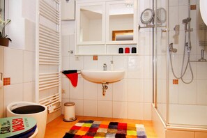 A bathroom with a sink, mirror, shower, and a colorful rug. - Wohnung in Rehm-flehde-bargen mit Einer Terrasse (Rehm-Flehde-Bargen)