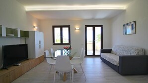 A modern living room with a flat-screen TV, a glass dining table with chairs, a sofa, and a painting on the wall. - Apartment on Costa Rei With Stunning Beaches (Muravera)