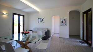 A modern dining area with a glass table, white chairs, and a vase of flowers. - Apartment on Costa Rei With Stunning Beaches (Muravera)