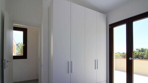 A bedroom with a large wardrobe, a bed with a blue cover, and a sliding glass door to a balcony. - Apartment on Costa Rei With Stunning Beaches (Muravera)