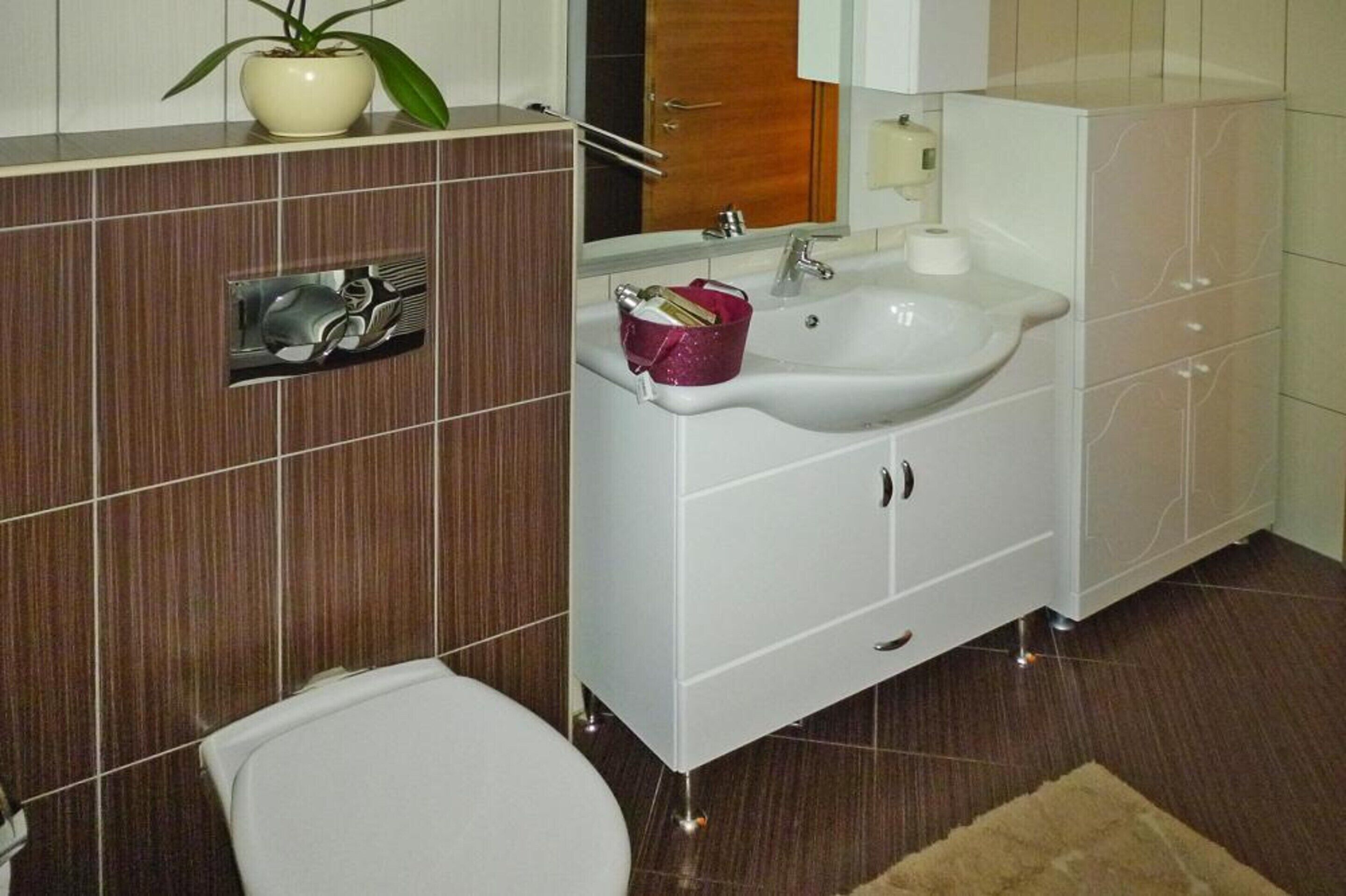 A bathroom with a white sink, mirror, and cabinet, a toilet, and a potted plant on the counter.
