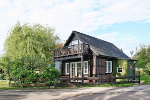 A traditional wooden house with a balcony, large windows, and a green door. - Ferienhaus Haffschein, Moenkebude (Monkebude)