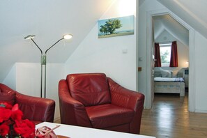 A room with a red leather chair, a floor lamp, and a painting of a tree on the wall. - Ferienhaus Haffschein, Moenkebude (Monkebude)