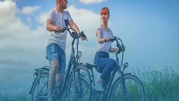 Two people on bicycles in a grassy field with a clear sky.