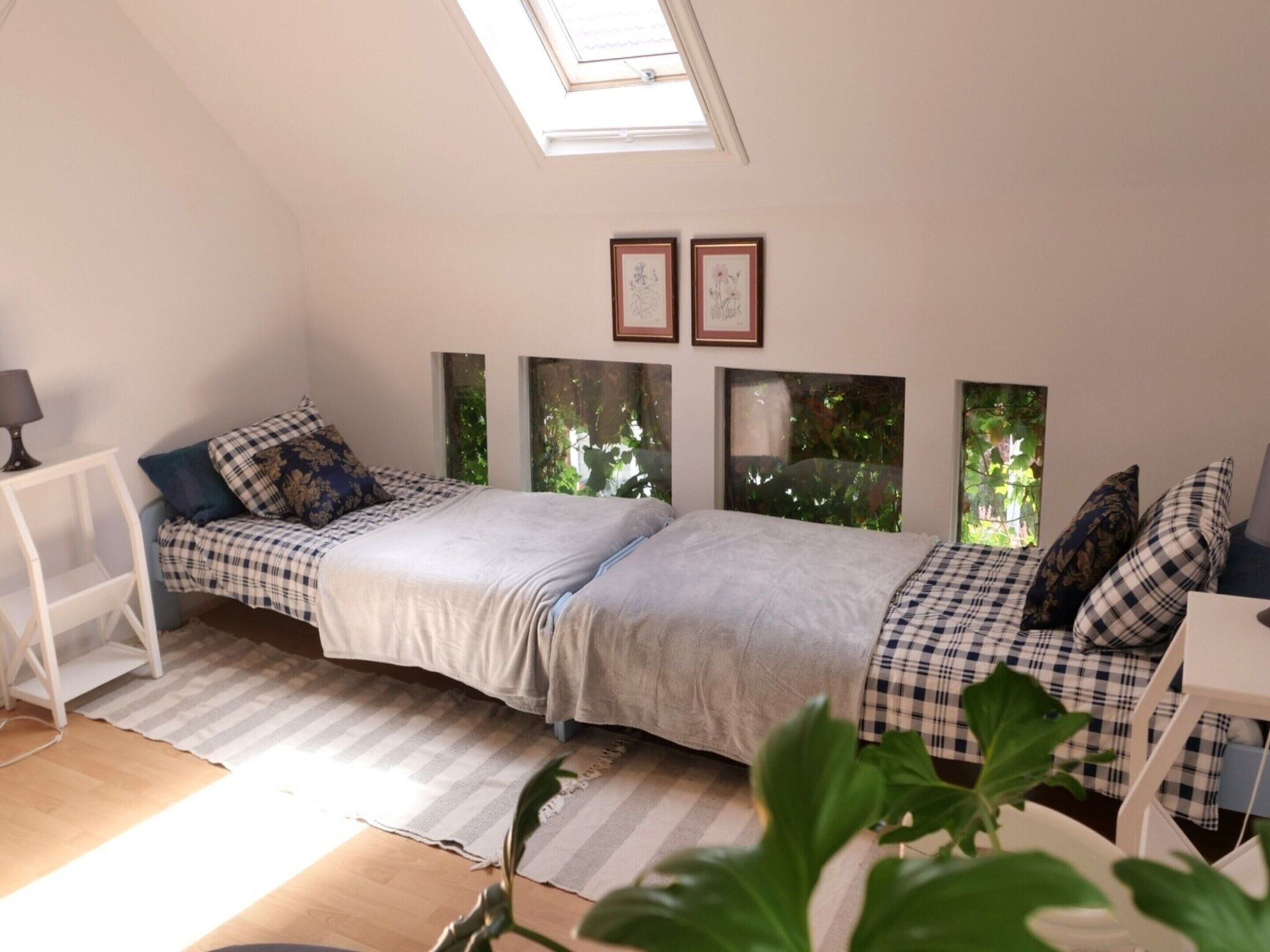 A bedroom with a bed, a bedside table, a lamp, and a window with a view of greenery.