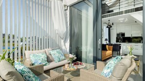 A modern outdoor living area with wicker furniture, a glass table, and a view into the kitchen. - Holiday Home With Whirlpool Bathtub, Wrzosowo (Kamien Pomorski)