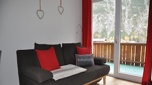 Una sala de estar moderna con un sofá gris, cojines rojos y grises, y suelo de madera.