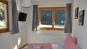 Un dormitorio con cama, ropa de cama a cuadros, una ventana con cortinas, un radiador y un televisor en la pared.