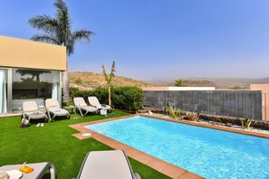 Un área de piscina moderna al aire libre con una vista despejada del paisaje circundante, incluyendo colinas y una palmera.