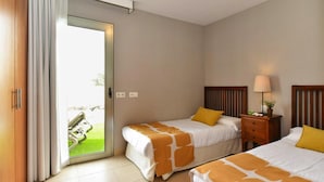 A hotel room with two beds, a sliding glass door to the outside, a bedside table with a lamp, and a small plant. - Holiday Home, Maspalomas (San Bartolomé de Tirajana)
