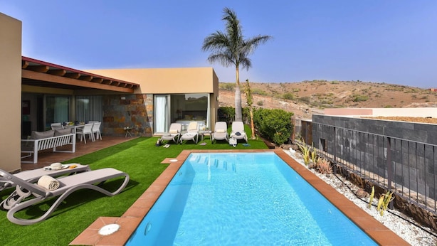 A modern pool area with lounge chairs, a small patio with outdoor furniture, and a view of the surrounding landscape. - Holiday Home, Maspalomas (San Bartolomé de Tirajana)