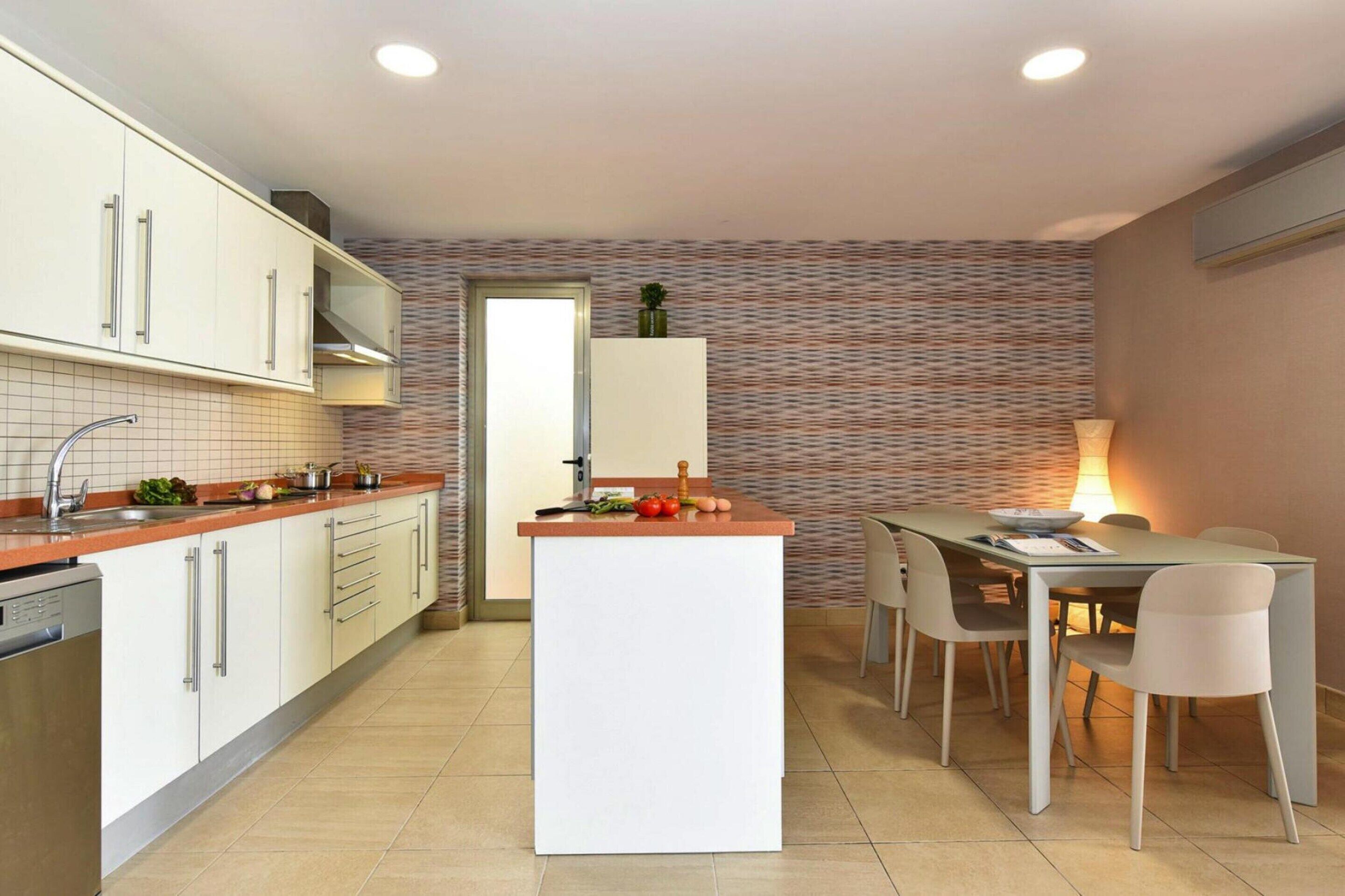 Une cuisine moderne avec des meubles blancs, un îlot central et un coin repas comprenant une table et des chaises.