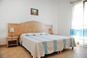 A bedroom with a wooden headboard, two bedside tables with lamps, a bed with a striped bedspread, a picture on the wall, and a window with curtains.