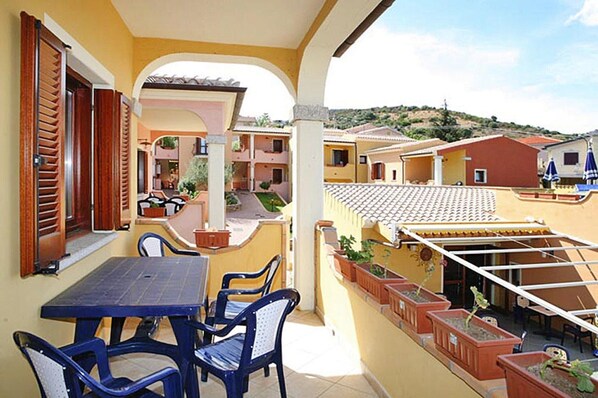 A terrace with a table and chairs, potted plants, and a view of neighboring buildings.