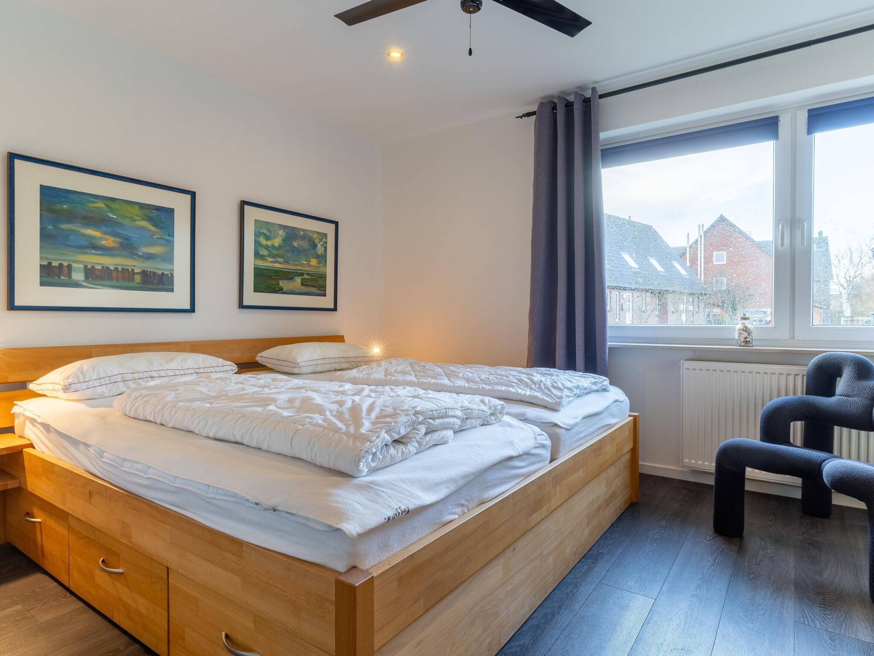 A bedroom with a wooden bed, two framed paintings, a window with curtains, and a radiator.