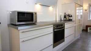 A modern kitchen with a microwave, oven, and wine bottles on the counter. - Ferienhaus fur bis zu 6 Personen, Am Wung in Husum (Husum)