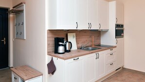 Uma cozinha compacta com armários brancos, bancada de madeira, cafeteira, pia e forno pequeno.