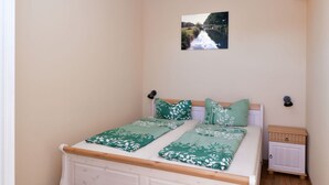 Quarto com cama, mesa de cabeceira, luminária na parede e quadro de um rio.