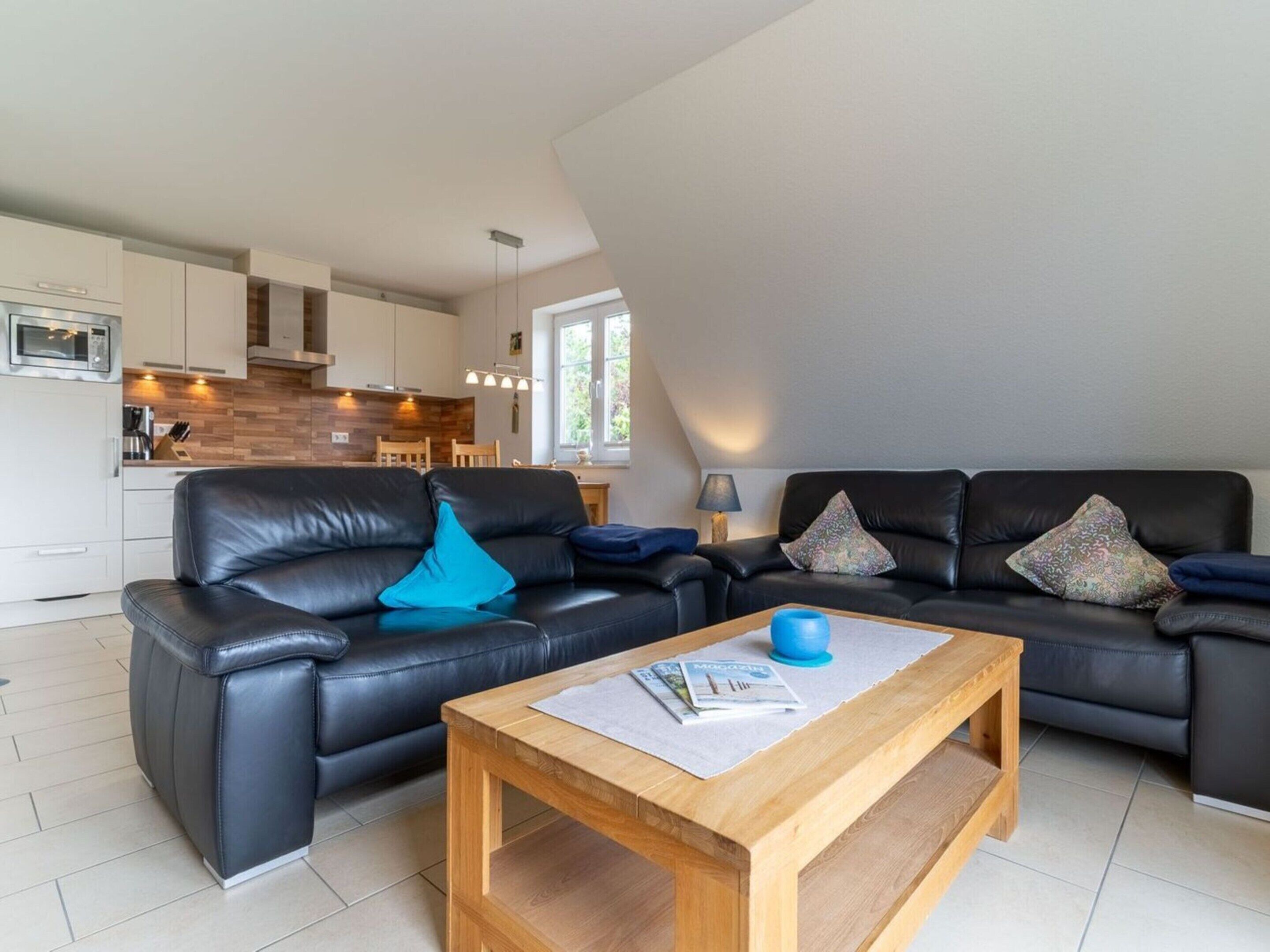 A modern living room with a black leather sofa, a wooden coffee table, and a kitchen in the background.