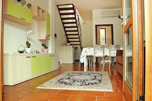 Une cuisine avec des meubles de couleur verte, un coin repas avec une table et des chaises, et un escalier.