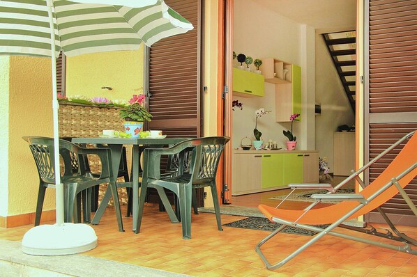 A dining area with a table and chairs, a striped umbrella, and a kitchen visible through an open door. - Apartment by Lake Como With Stunning Views (Lezzeno)