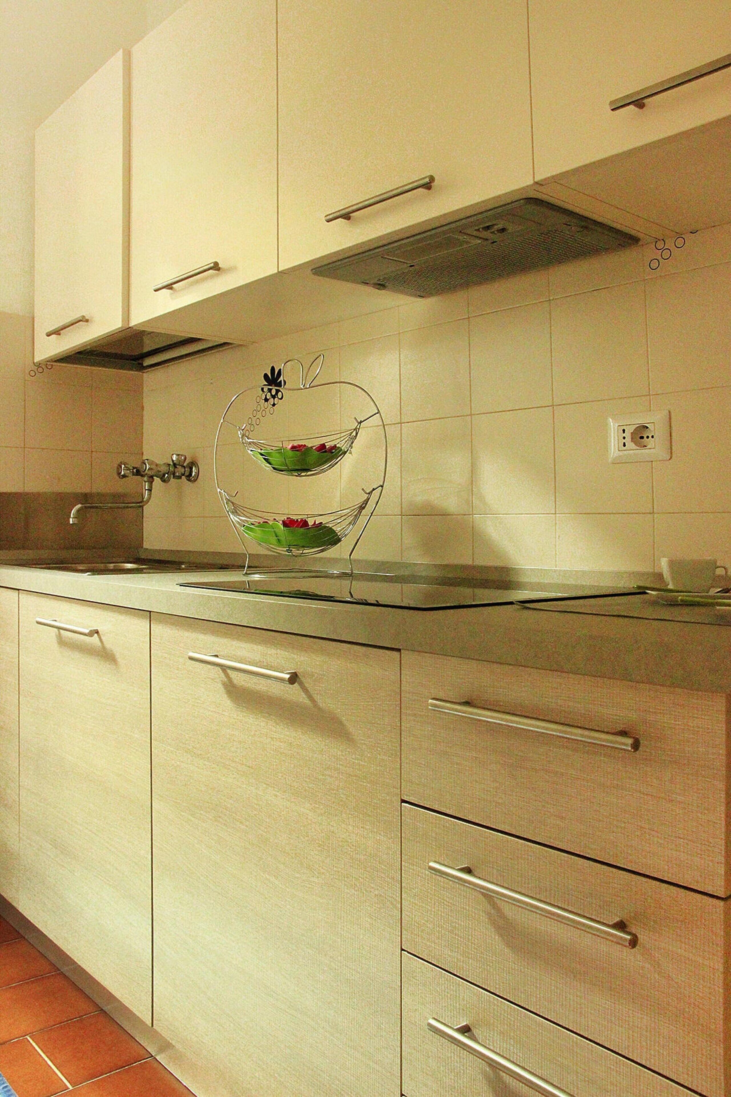 A kitchen with white cabinets, a stainless steel countertop, and a double-tiered glass bowl on the counter.