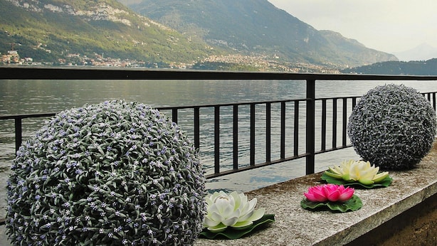 Vista de un lago con montañas, barandilla, esferas decorativas y flores de loto.