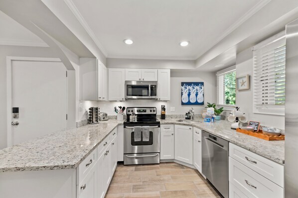 A modern kitchen with white cabinetry, stainless steel appliances, granite countertops, and a window with blinds. - Centrally Located 2BR/2Bath Villa in Kiawah Island, SC --
5 min from the Beach! (Kiawah Island)