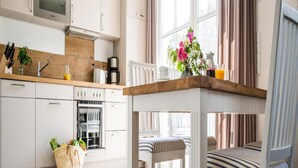 A modern kitchen with white cabinets, a wooden countertop, and a dining area with striped chairs. - Ferienwohnung, Zingst (Zingst)