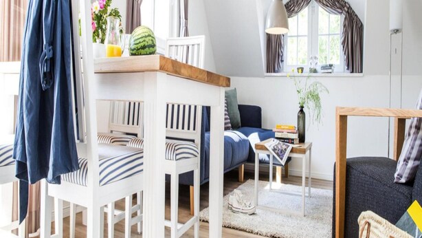 A modern living room with a high ceiling, a dining area with white furniture, and a cozy seating area with a sofa and armchairs. - Ferienwohnung, Zingst (Zingst)