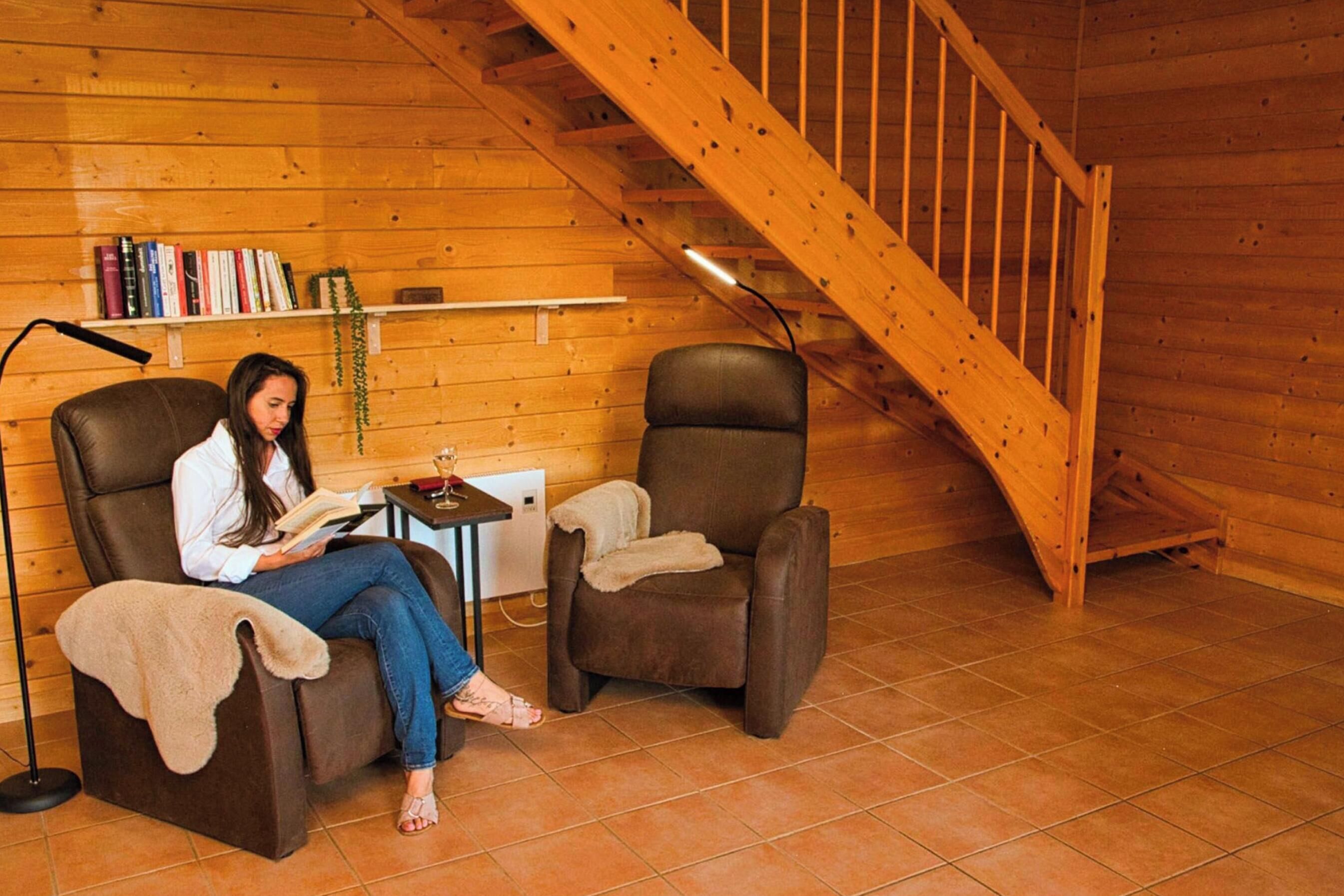 Una habitación acogedora con una escalera de madera, dos sillones reclinables, una mesita y una estantería llena de libros.