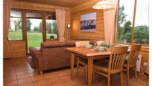 Uma cabana de madeira com uma mesa de jantar posta para dois, um sofá e uma grande janela com vista para o exterior.
