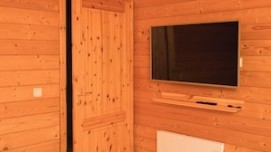 Quarto com painéis de madeira, uma porta, uma televisão fixada na parede e um radiador branco.