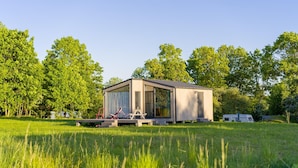 A modern, single-story house with a large glass door, surrounded by a grassy field and trees. - Cottage in the Middle of Nature, Pilwa (Wegorzewo)
