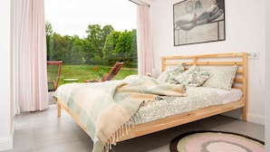 A bedroom with a wooden bed, a view of the outdoors, and a framed artwork on the wall. - Cottage in the Middle of Nature, Pilwa (Wegorzewo)
