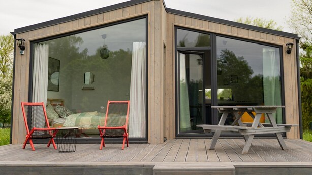 A modern cabin with large glass windows, a wooden deck, and outdoor seating. - Cottage in the Middle of Nature, Pilwa (Wegorzewo)