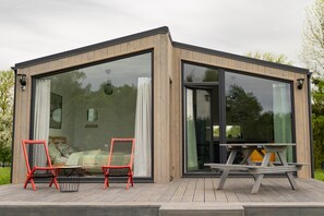 A modern cabin with large glass windows, a wooden deck, and outdoor seating. - Cottage in the Middle of Nature, Pilwa (Wegorzewo)
