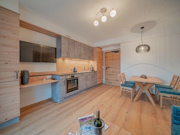A modern kitchen with wooden cabinets, a built-in oven, and a dining area with a wooden table and chairs. - Chalet in Brixental (Brixen im Thale)