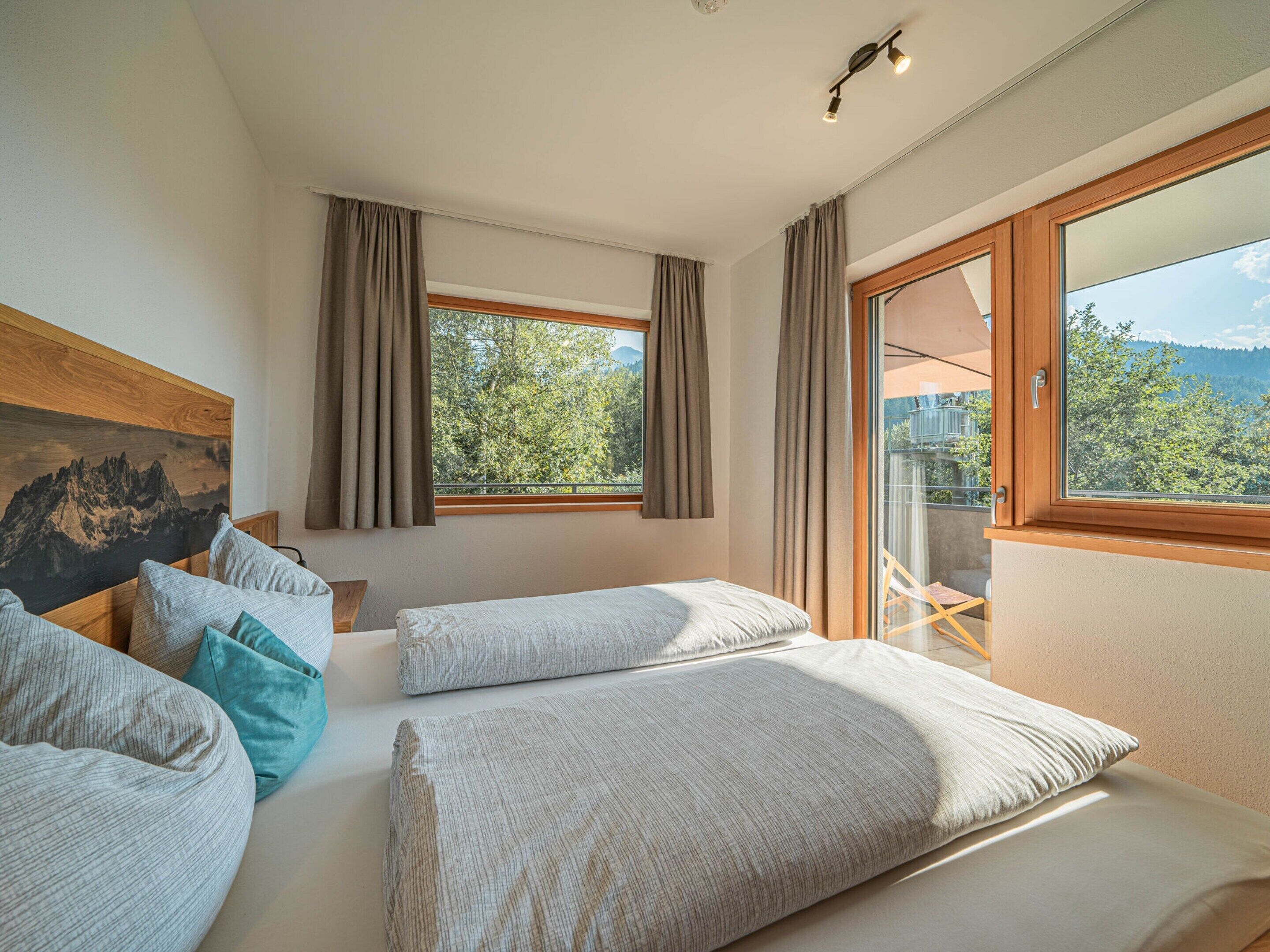 Une chambre avec deux lits, une grande fenêtre et une vue sur les arbres et les montagnes.