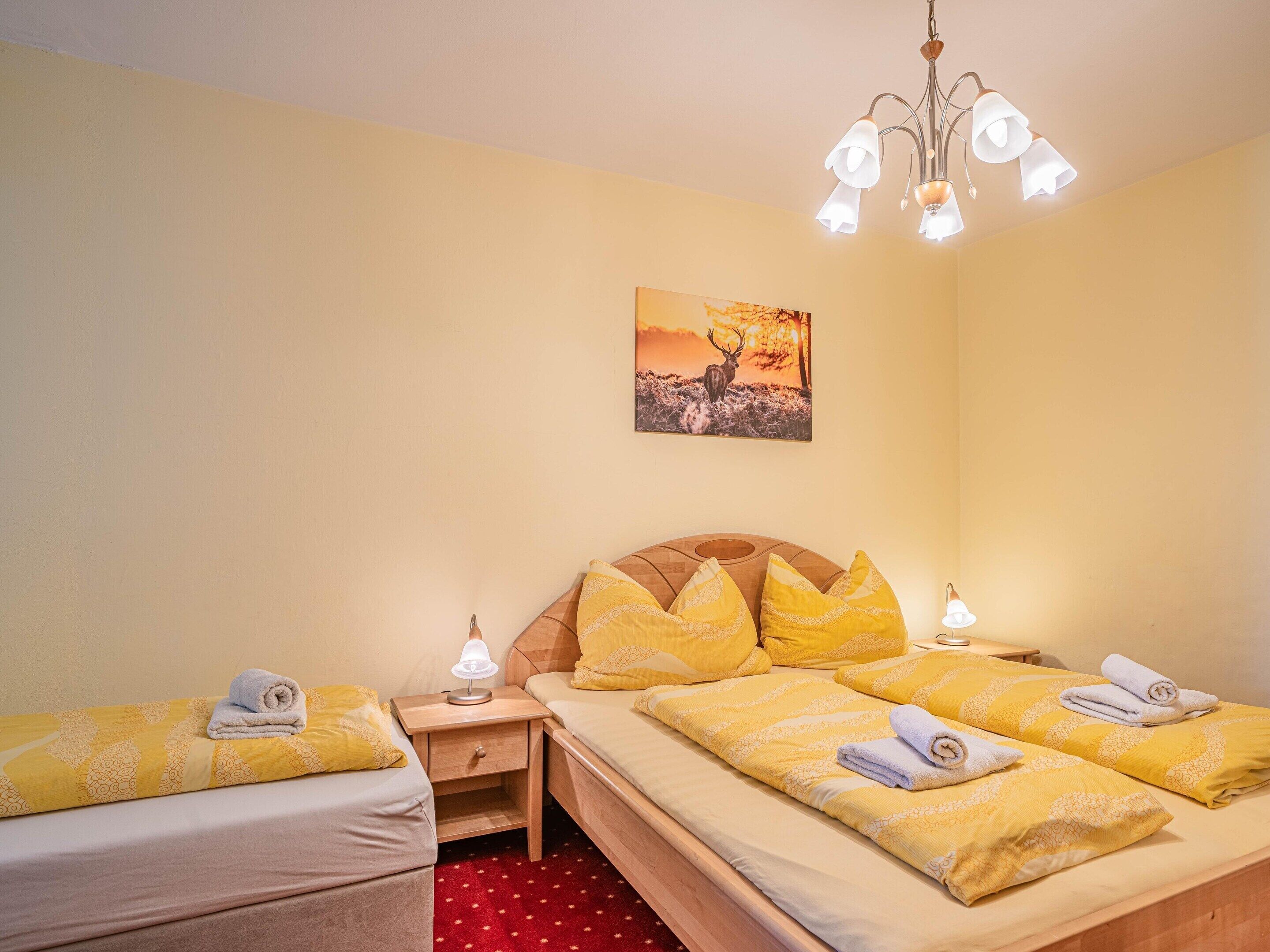 A hotel room with two beds, a wooden headboard, a nightstand with a lamp, and a painting on the wall.