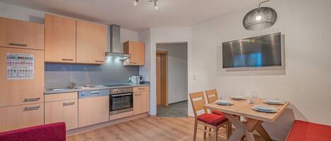 A compact kitchen with wooden cabinets, a built-in oven, and a dining area with a table and chairs.