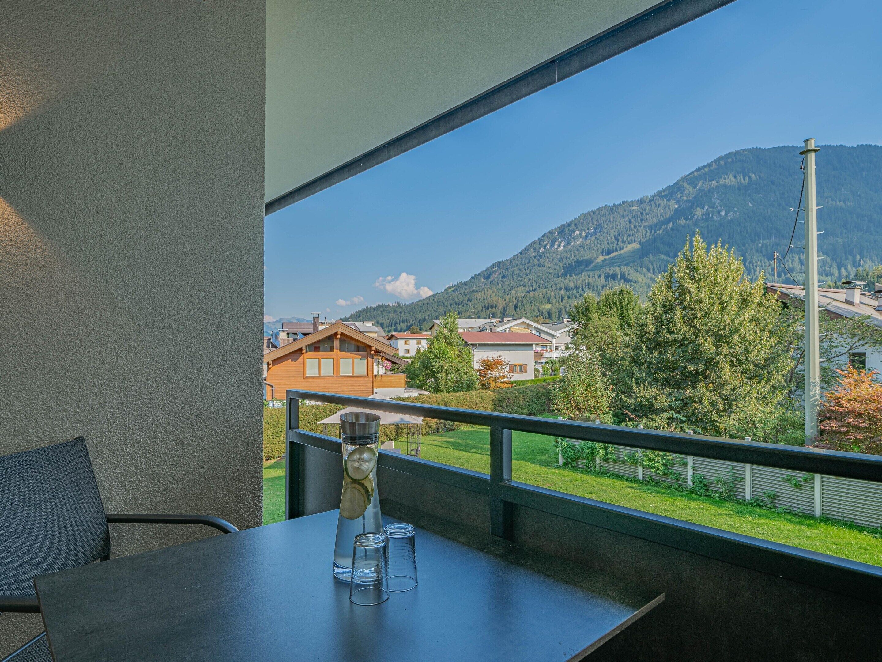 A balcony with a table, chairs, and a clear view of a mountain and houses.