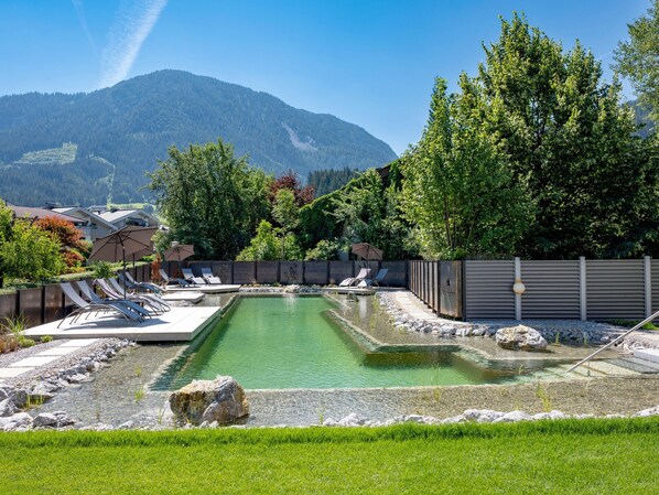 A pool area with lounge chairs and a mountain backdrop. - Chalet in Brixental (Brixen im Thale)