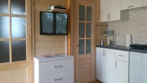 A compact kitchen with wooden walls, a built-in TV, white cabinets, and a tiled backsplash. - Holiday Homes Close to the Seaside Beach (Ustronie Morskie)