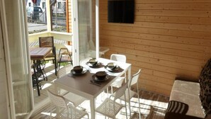 A wooden interior with a dining table set for four, white chairs, and a television mounted on the wall. - Holiday Homes Close to the Seaside Beach (Ustronie Morskie)