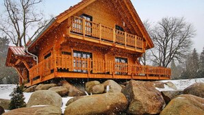 A wooden cabin with a balcony, surrounded by rocks and snow. - Ferienhaus, Schierke (Wernigerode)