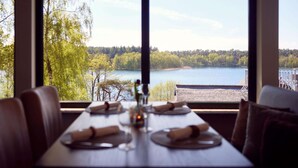 Una mesa de comedor con vistas a un lago y un bosque a través de amplios ventanales.